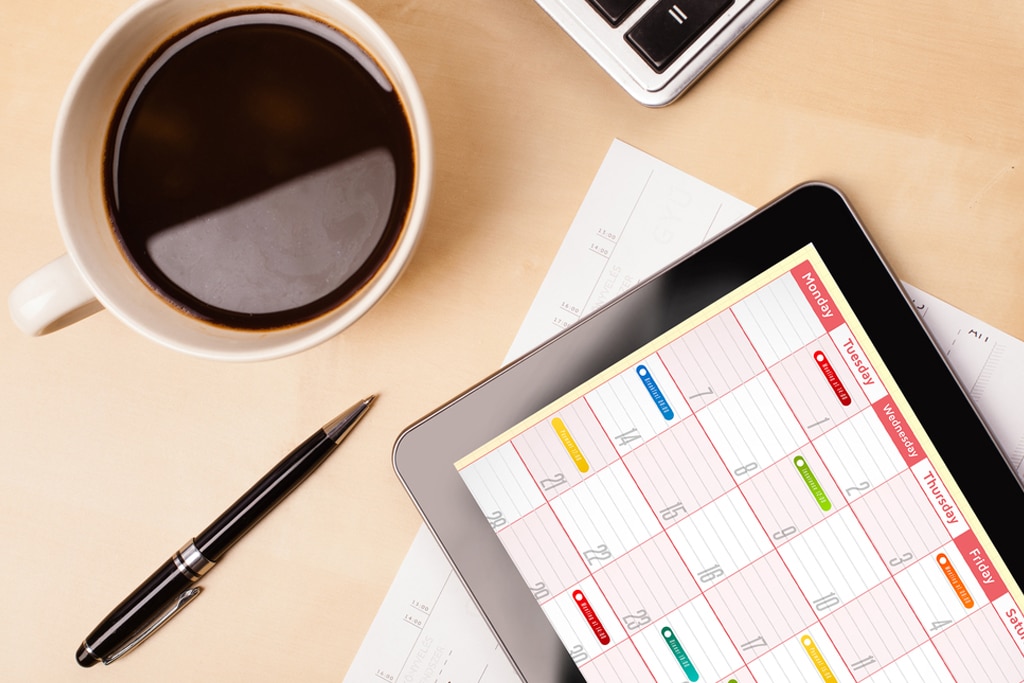 Workplace with tablet pc showing calendar and a cup of coffee on a wooden work table close-up