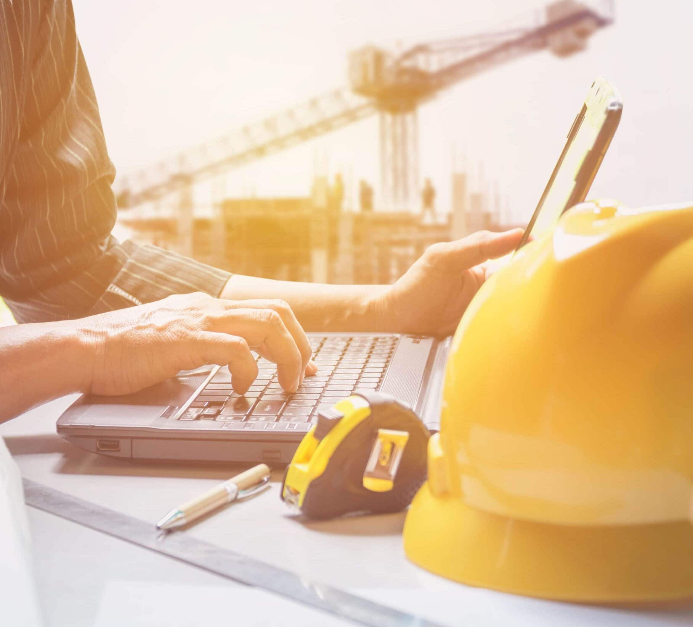 engineer using laptop with a yellow helmet in the foreground
