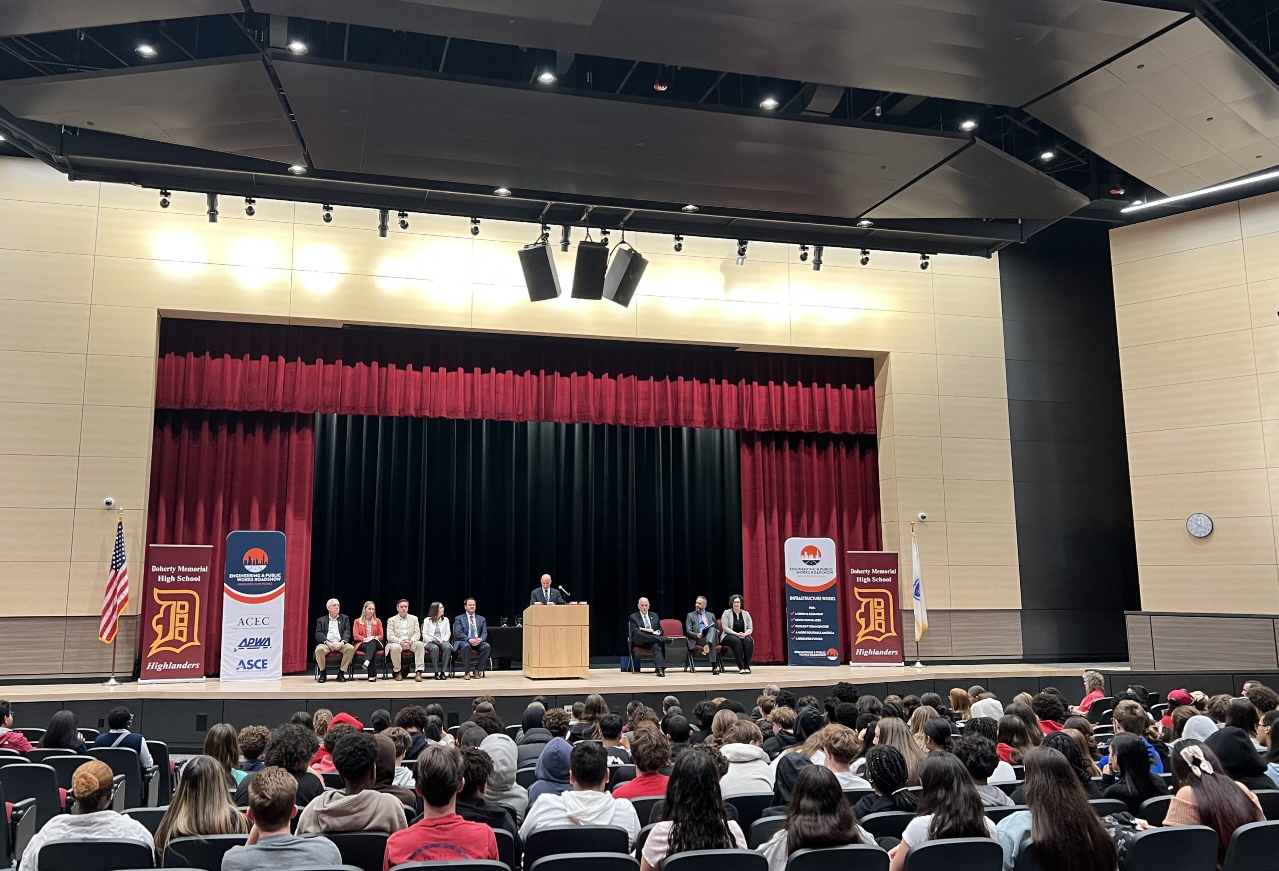 An auditorum with a speaker on stage and students sitting in the seats. 