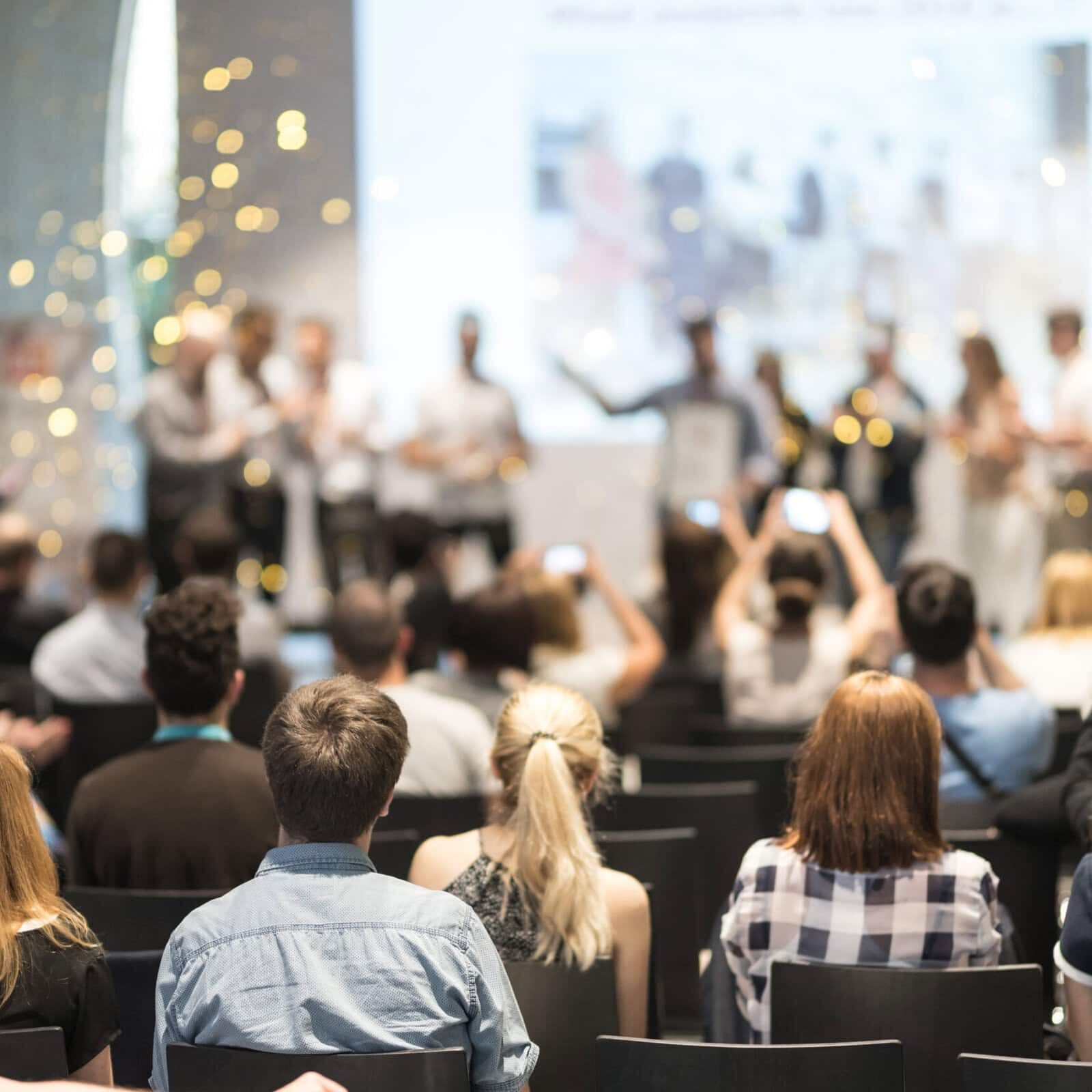 Young business team receiving award at best business project competition event. Business and entrepreneurship award ceremony theme. Focus on unrecognizable people in audience.