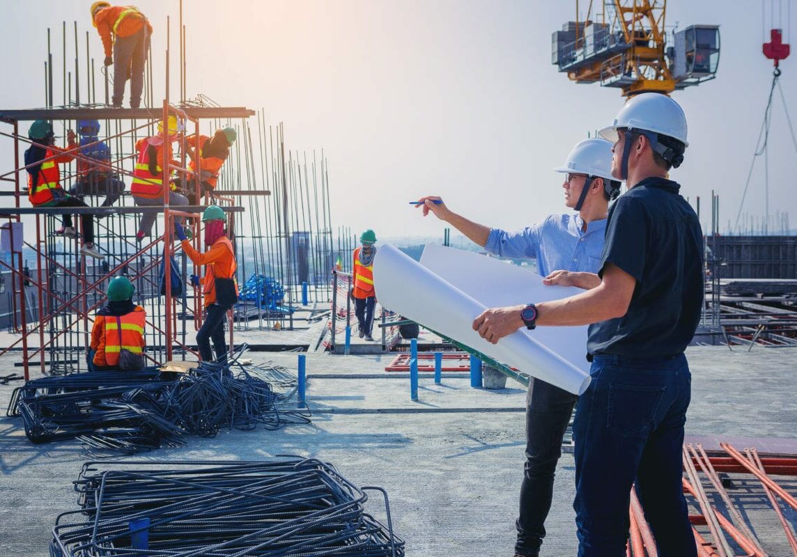 Structural engineer and architect working with blueprints discuss at the outdoors construction site.