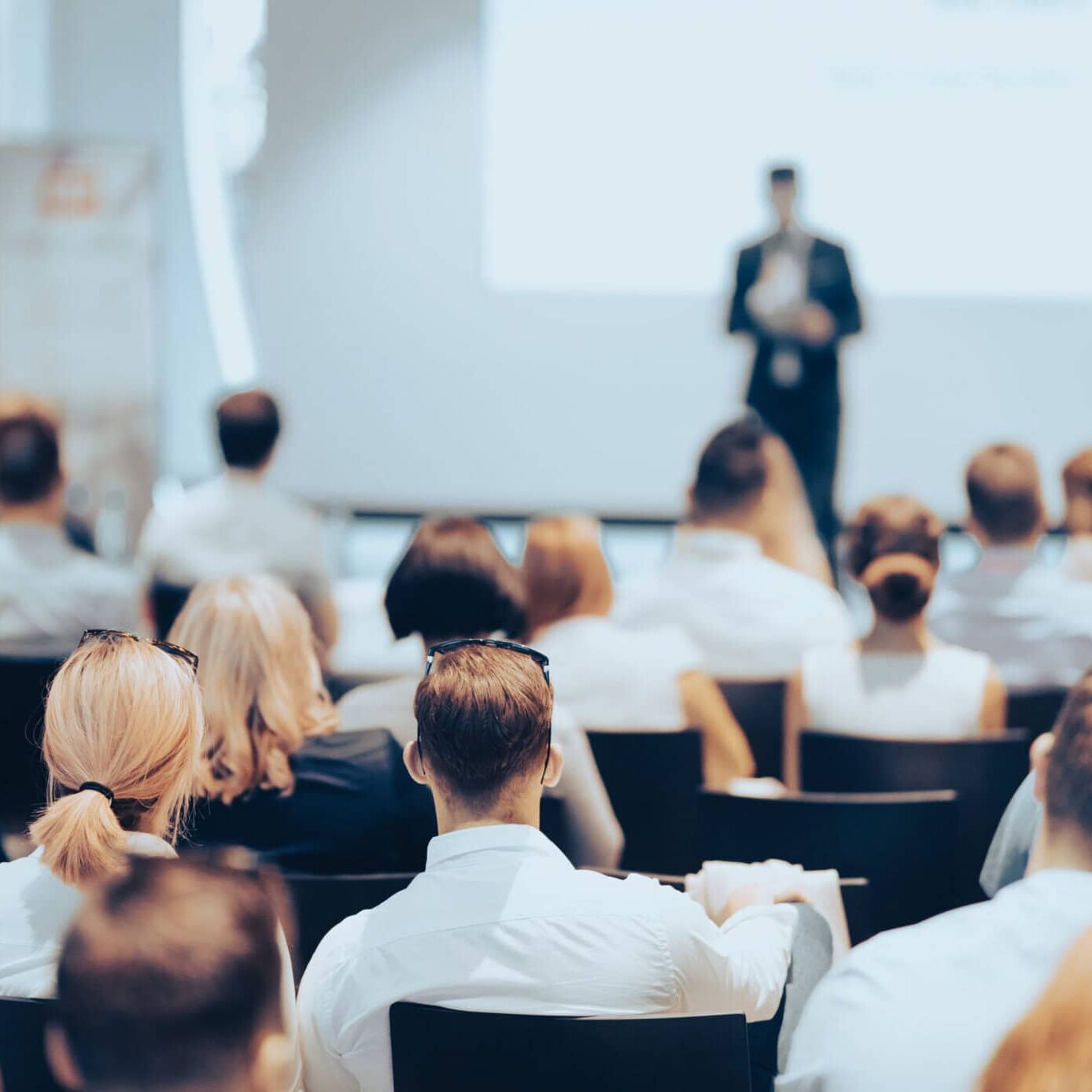 Speaker giving a talk in conference hall at business event. Rear view of unrecognizable people in audience at the conference hall. Business and entrepreneurship concept.
