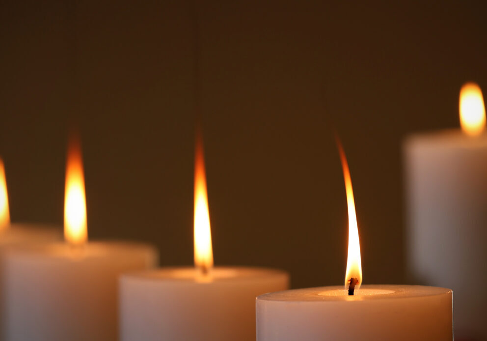 5 large white wax candles burning with long orange yellow flames. Five candle arrangement with a dark background.
