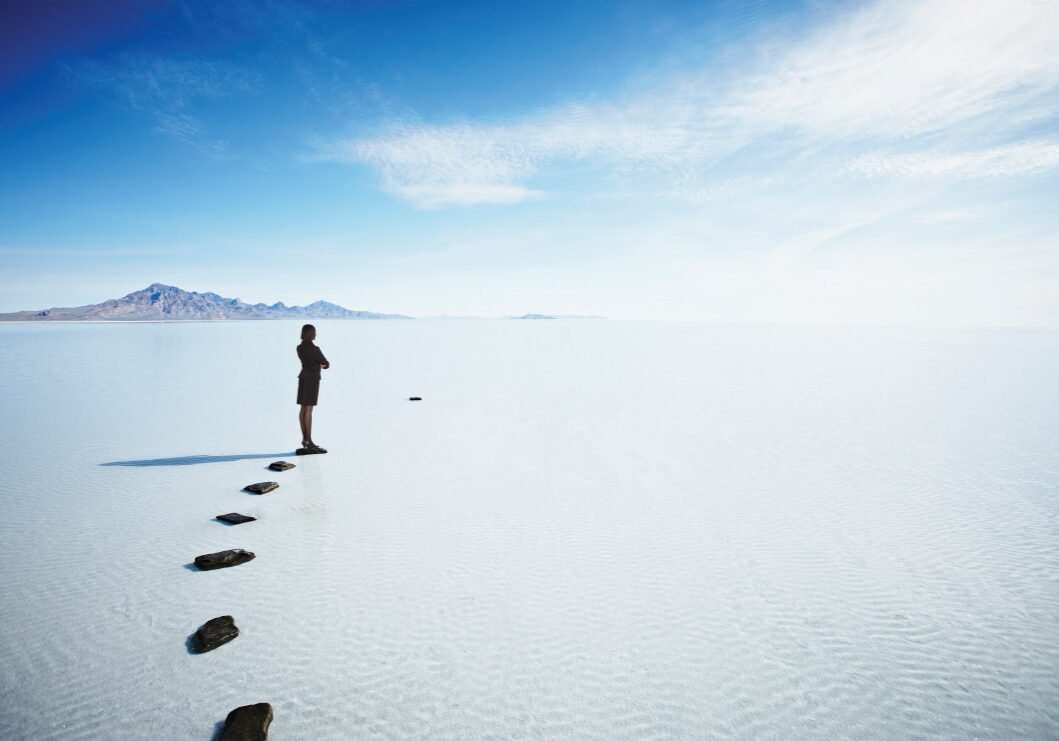 Businessman standing on stone pathway in lake looking at large gap between stones