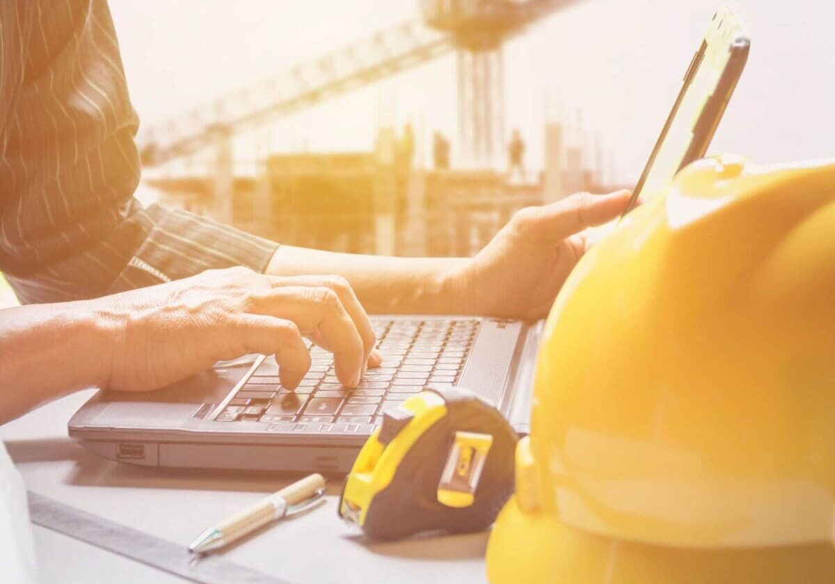 engineer using laptop with a yellow helmet in the foreground